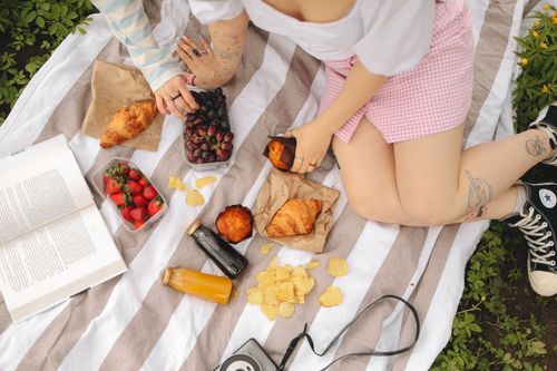 Free Overhead view of a vibrant picnic scene with fruits, pastries, and a book on a striped blanket. Stock Photo