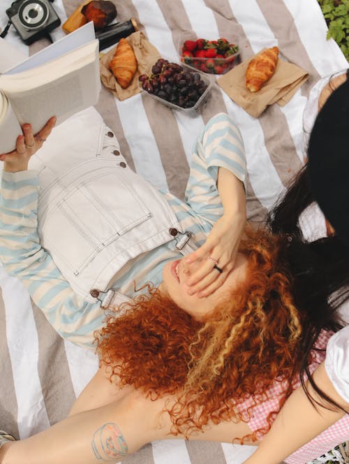 Free Curly Haired Woman Reading a Book While Lying on Picnic Blanket  Stock Photo