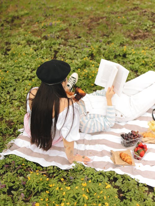 Women Lying on a Blanket Reading a Book During a Picnic