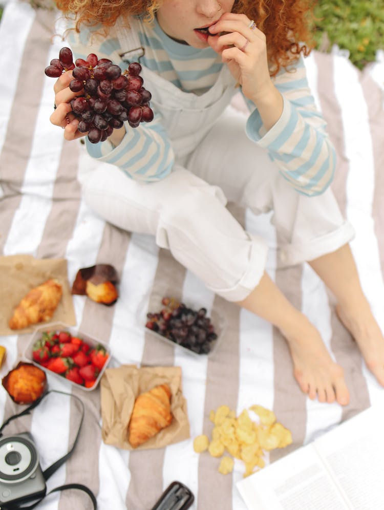 Woman Sitting On A Picnic Blanket While Eating Grapes