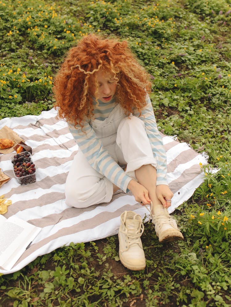 A Woman Sitting On A Picnic Blanket While Tying Her Shoes