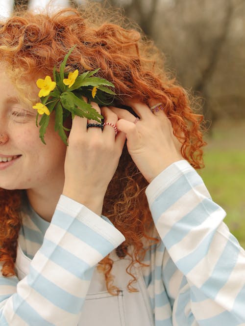 A Woman in Curly Hair Clipping the Yellow Flowers with Green Leaves on Her Ear