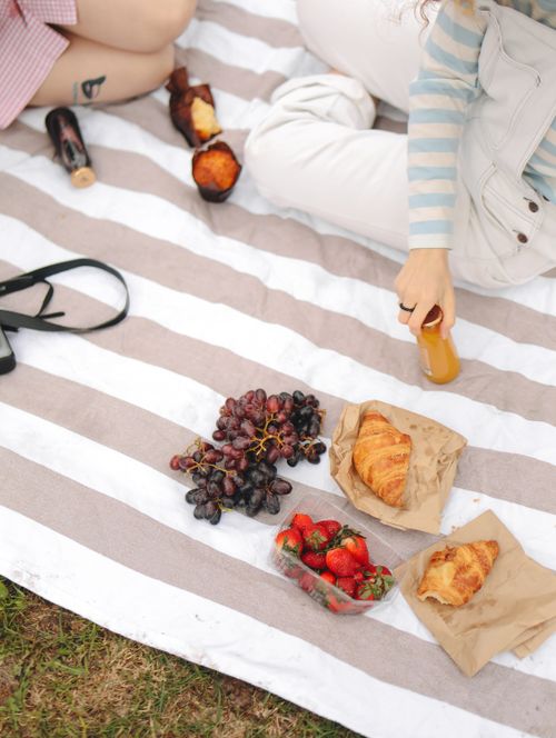 Free Relaxing outdoor picnic with grapes, strawberries, croissants, and orange juice on a striped blanket. Stock Photo