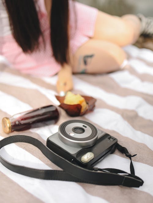 Black Instax Near Bottle of Juice and Bread on a Picnic Blanket
