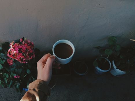 A cozy outdoor moment captured with a hand holding a coffee cup near vibrant flowers.