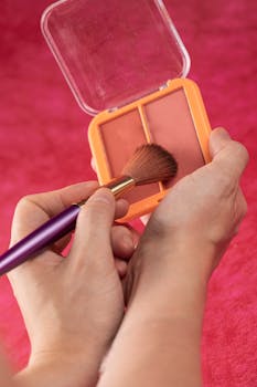 Hands applying blush with a makeup brush on a red background.