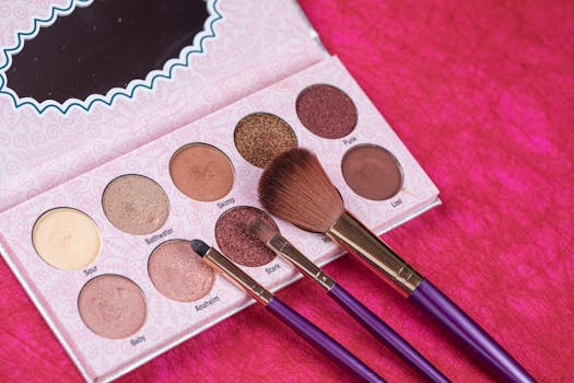 A detailed close-up of an eye shadow palette with makeup brushes on a vibrant pink fabric background.