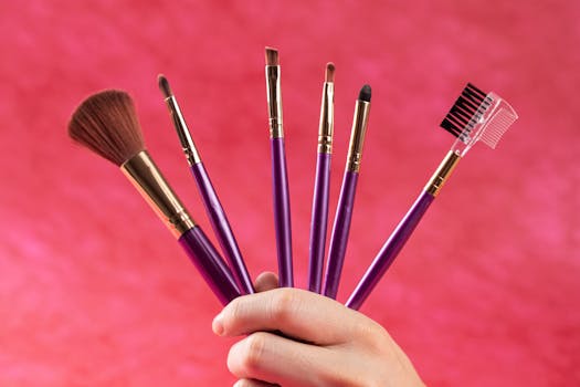 A set of makeup brushes held in hand with a vibrant pink backdrop, showcasing beauty tools.