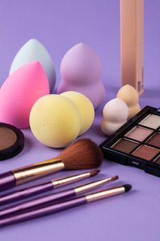 Colorful arrangement of beauty tools including brushes and sponges on a purple surface.