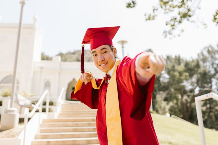 A Man In Red Academic Regalia Smiling While Wearing Mortarboard