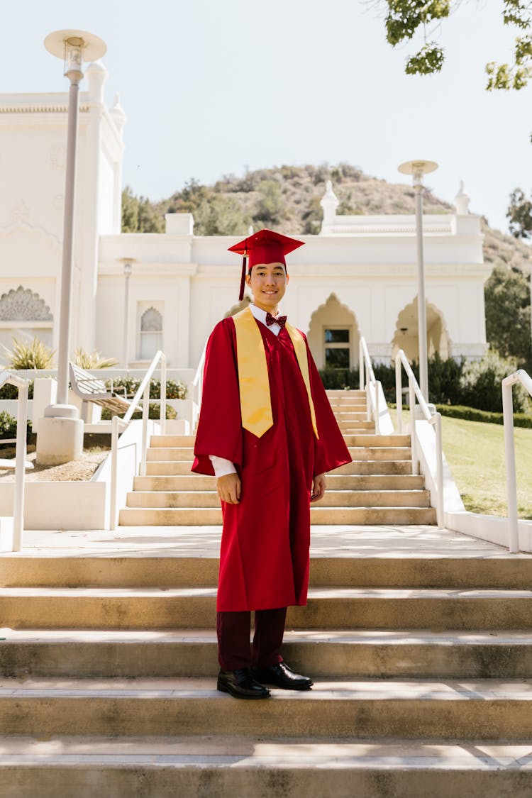 A Man In Red Academic Regalia Standing On A Concrete Stairs