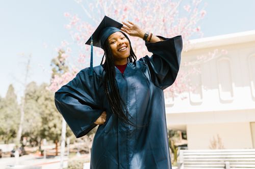 Free A joyful graduate poses outdoors in a blue cap and gown, celebrating success. Stock Photo