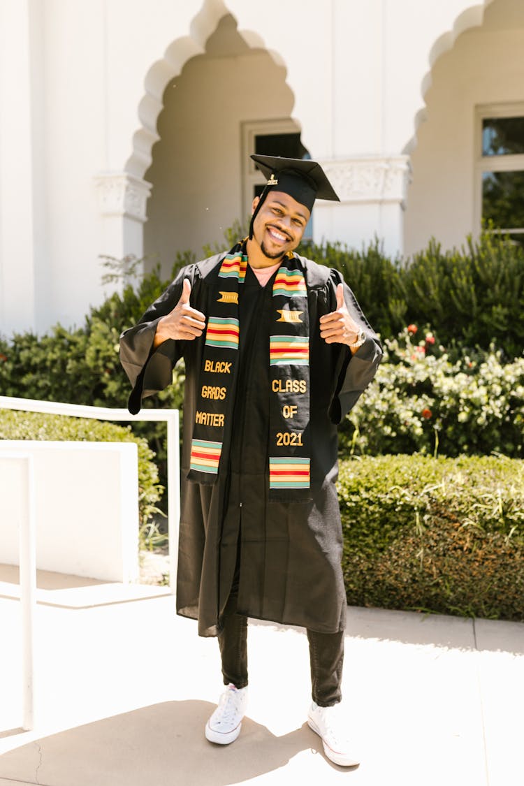 Man Wearing Black Graduation Gown And Cap Smiling