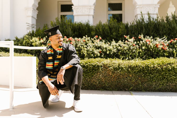 A Man In Black Academic Regalia Sitting On The Street