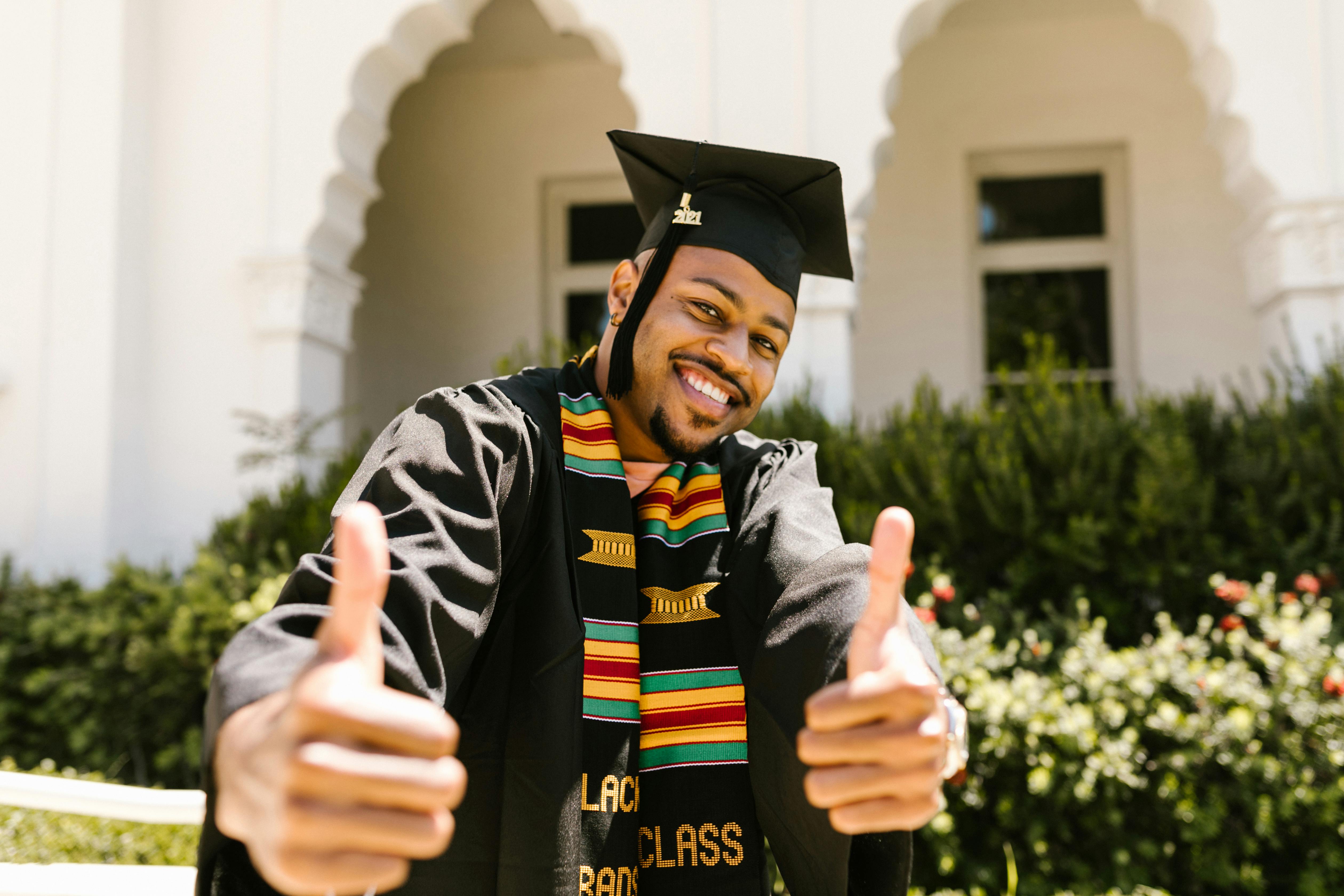 A joyful graduate with a kente stole gives thumbs up, celebrating his success.