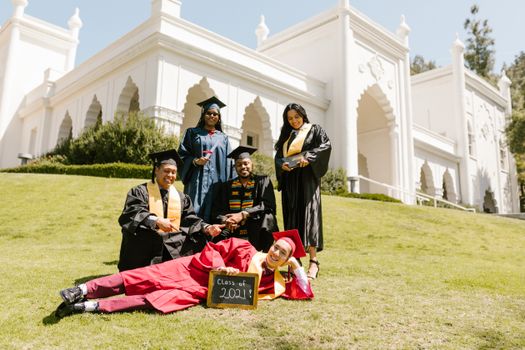 Graduates celebrating in caps and gowns on a sunny day, posing in front of a historical building.