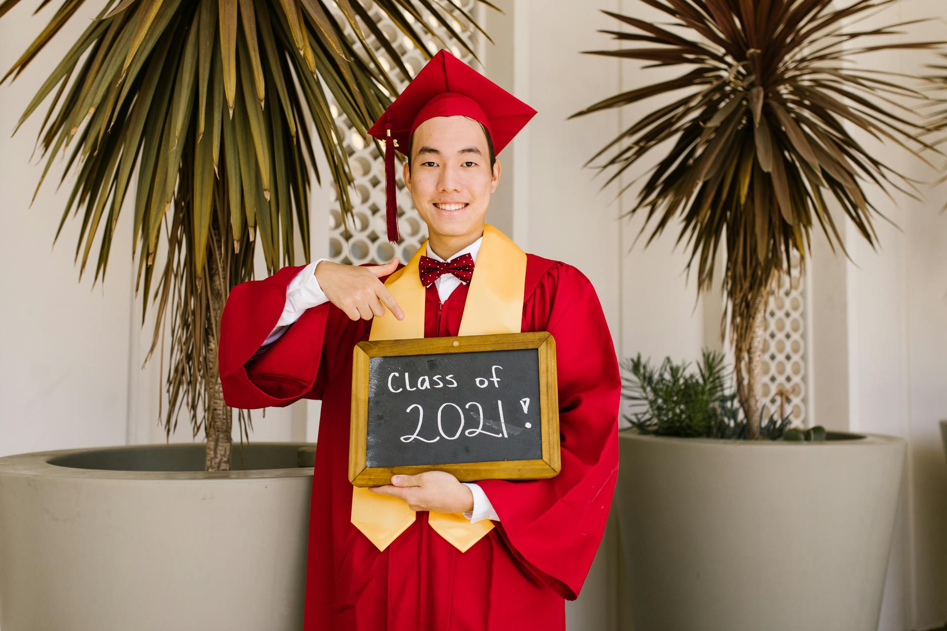 A Man in Red Academic Regalia Smiling while Holding a Mini Blackboard