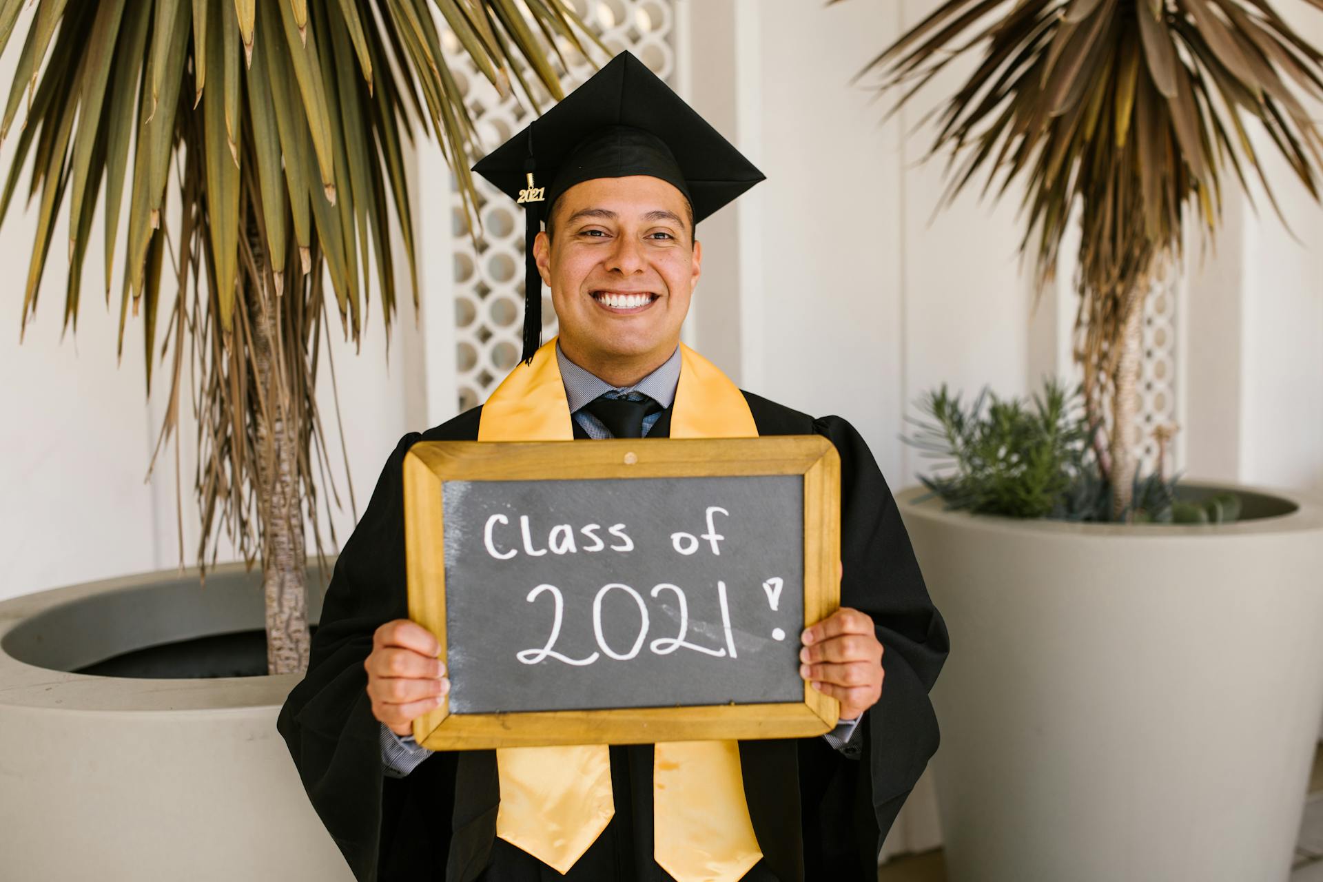 Smiling male graduate holding a Class of 2021 sign in cap and gown.