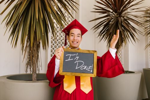 Free Smiling graduate in red gown holding chalkboard that reads 'I'm Done!' outdoors. Stock Photo