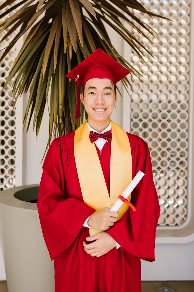 A Man In Red Graduation Gown Smiling