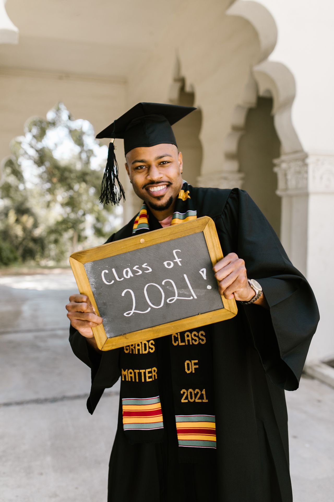 African American man in graduation cap and gown holding diploma board smiling