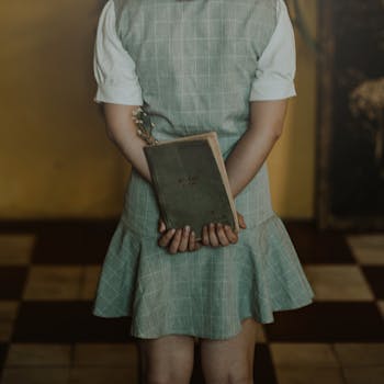 一名年轻女子穿着复古连衣裙，背着书站在室内