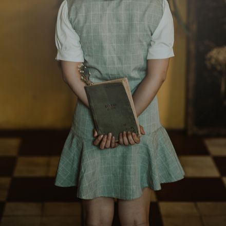 Woman in a checked linen pinafore dress holding a book — photo by Min An on Pexels