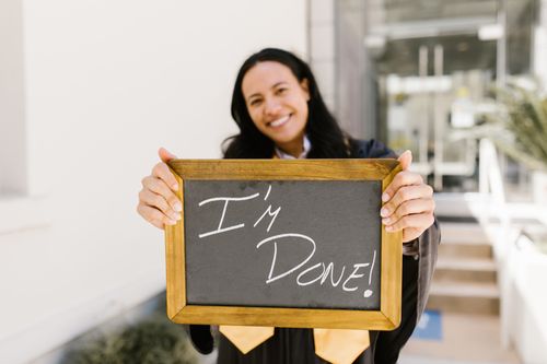 Free A happy graduate outdoors holding a chalkboard sign that reads 'I'm Done'. Perfect for celebrating success. Stock Photo