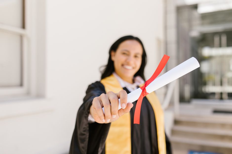 Graduate holding a diploma outdoors, smiling