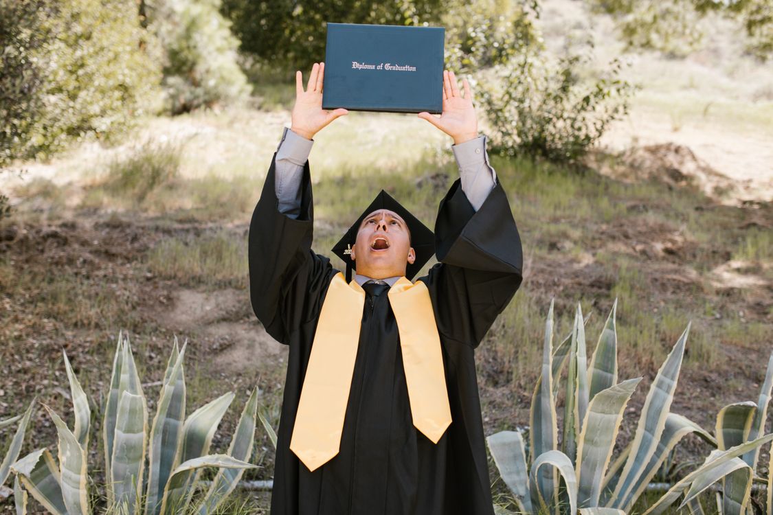 Student in a Graduation Gown Holding Up his Diploma · Free Stock Photo