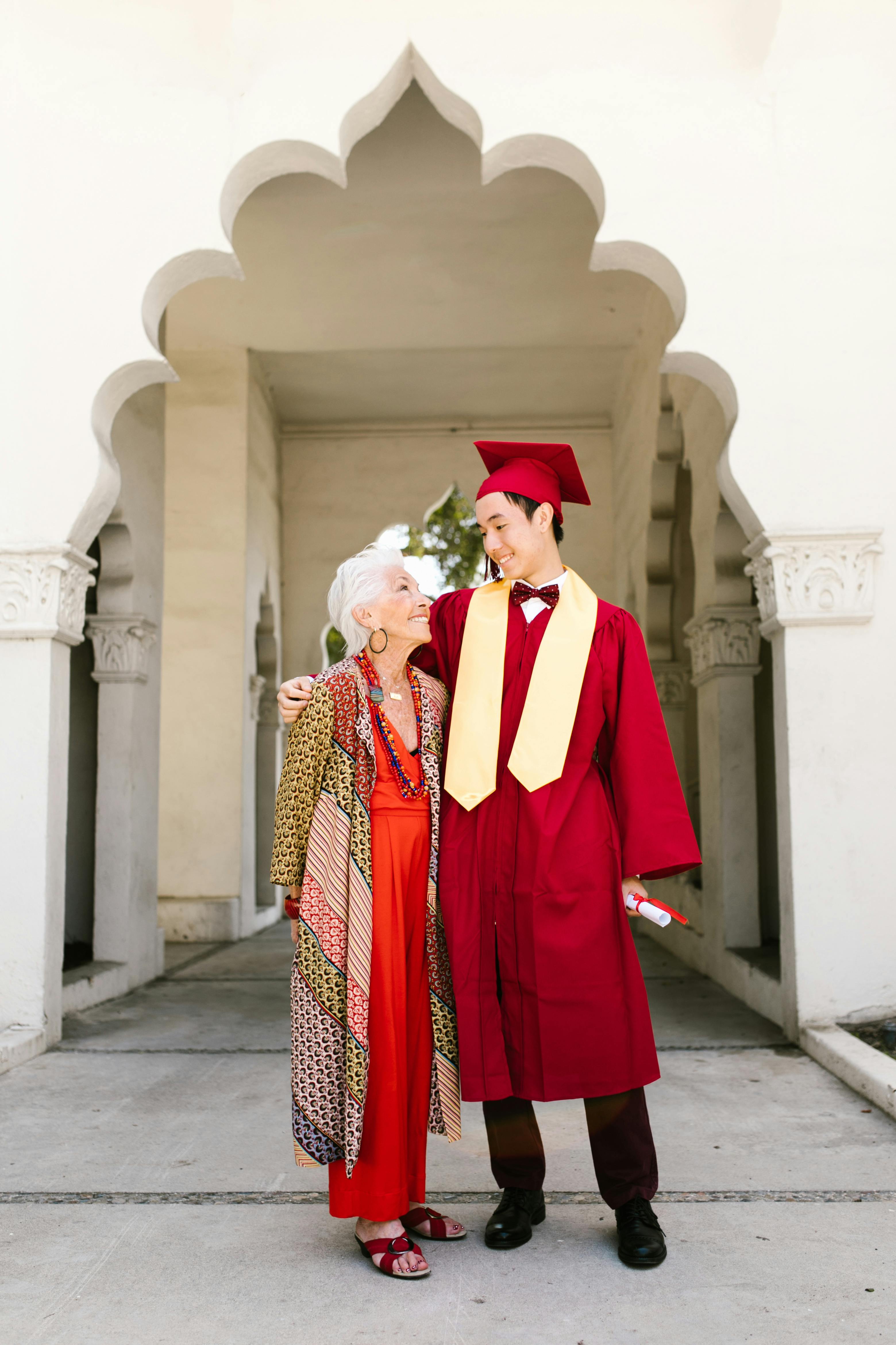 an elderly woman and a graduate in a red graduation gown