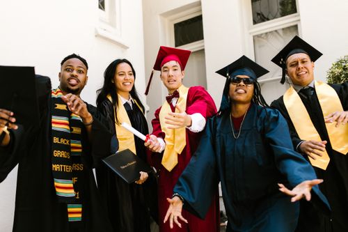Free Joyful graduates in academic gowns celebrate their achievement outdoors. Stock Photo