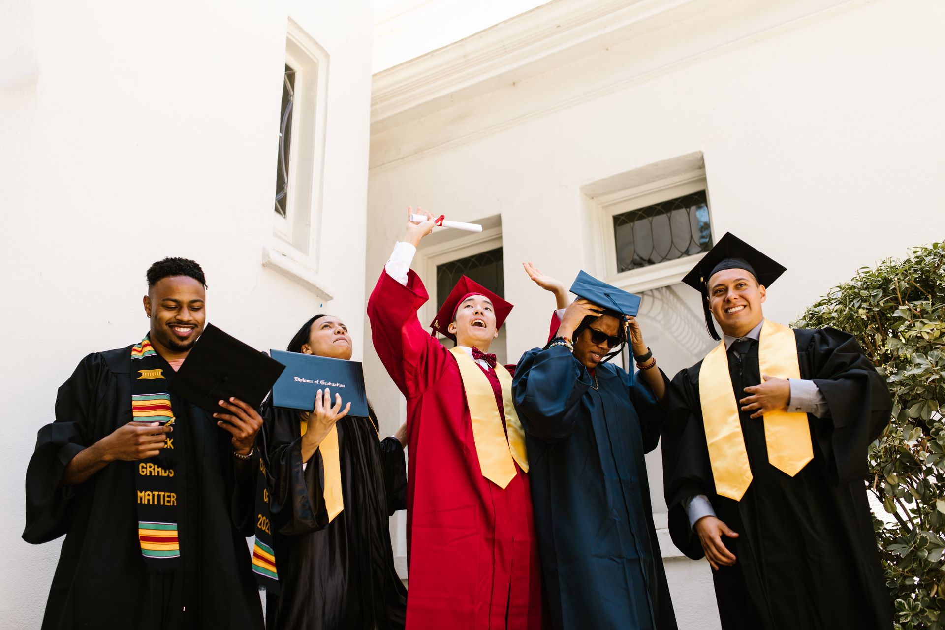 Group of graduates celebrating their achievements outdoors, wearing caps and gowns.