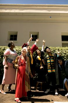 Graduates and an elderly woman celebrating outdoors under a sunny sky.