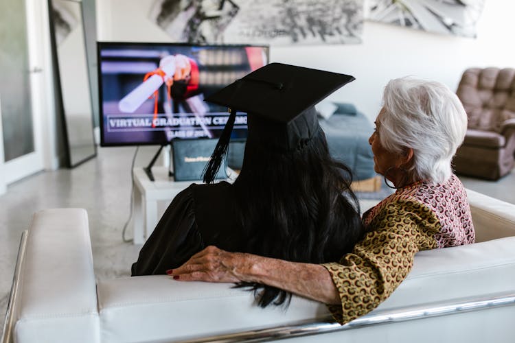 Back View Shot Of A Grandmother Sitting Beside Her Granddaughter Wearing Black Graduation Cap