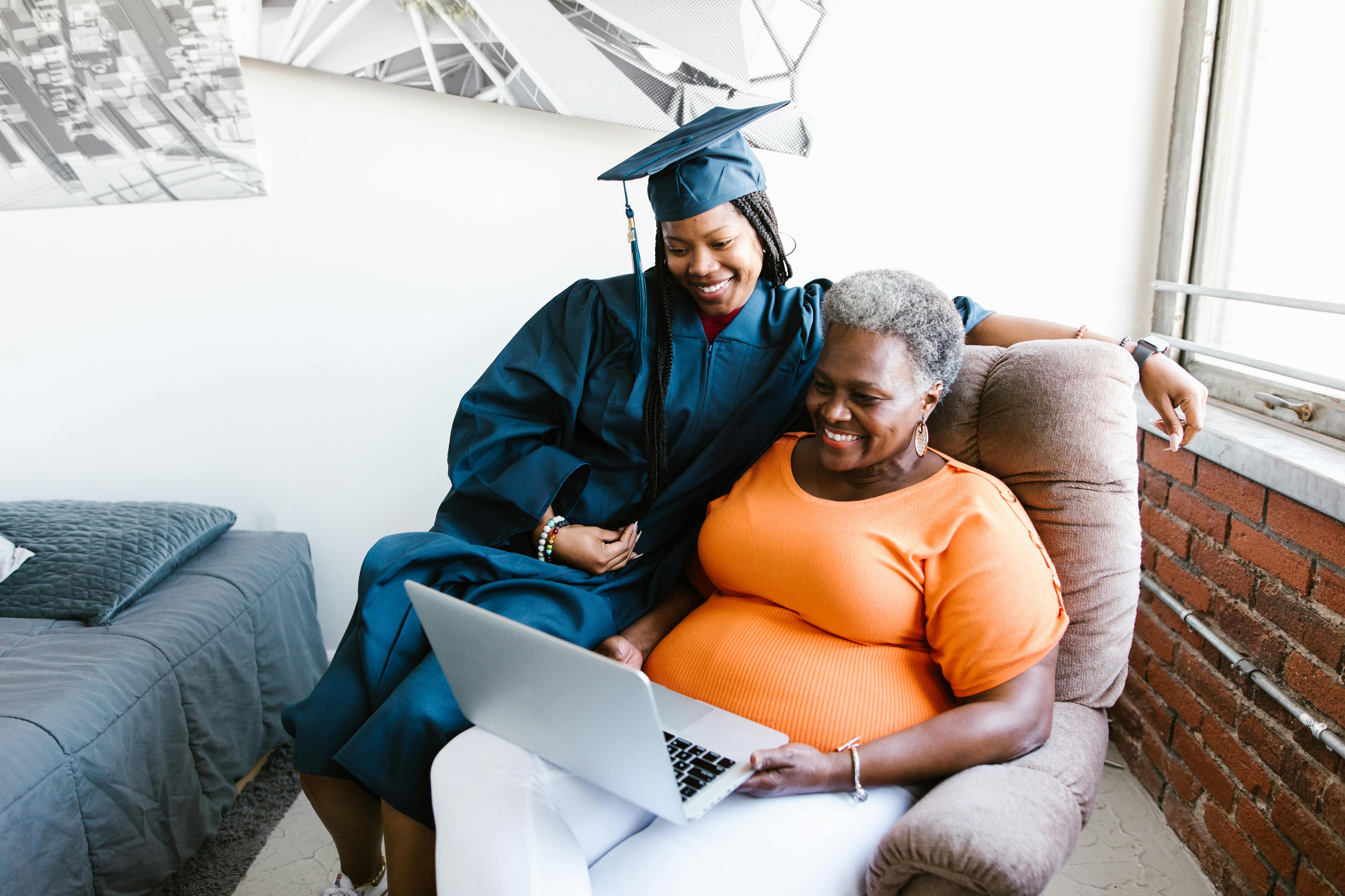 Graduate and family member sharing a heartfelt moment on a laptop, celebrating academic achievement.