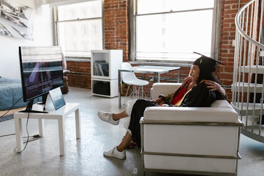 Two women celebrating a virtual graduation at home in a cozy apartment setting.