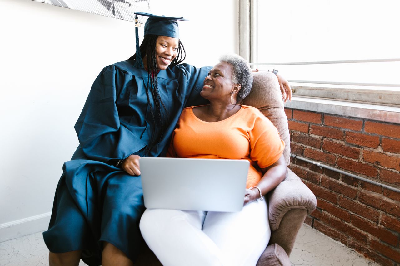 a graduate hugging her mom on a chair, browsing their online gallery on her laptop