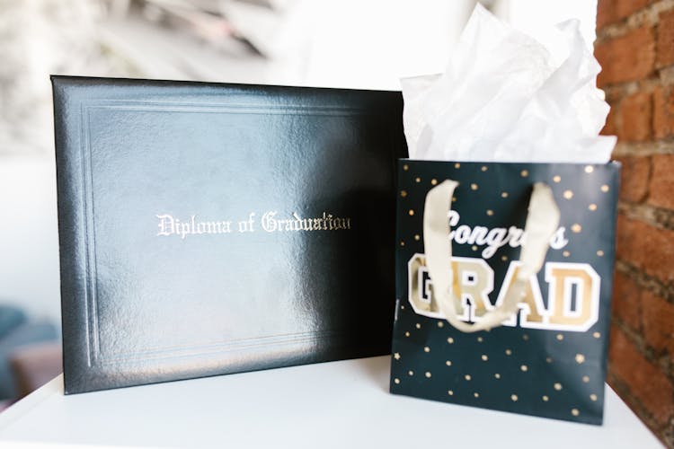 A Diploma Holder Beside A Gift