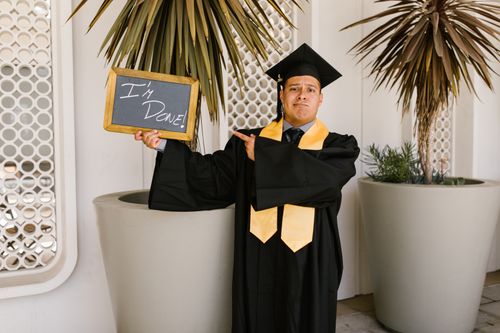 Free Adult male graduate in cap and gown holding 'I'm Done!' sign outdoors. Stock Photo