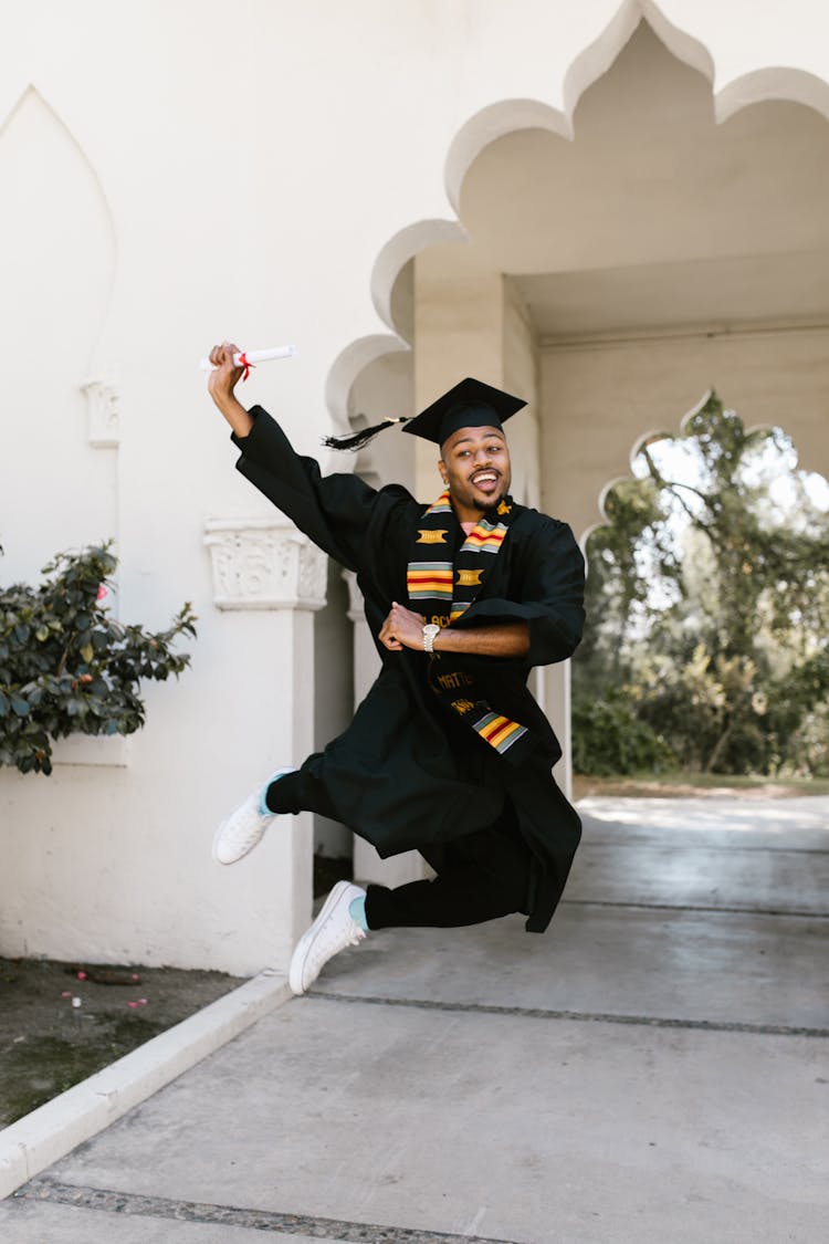 A Graduate Wearing A Graduation Cap Jumping 