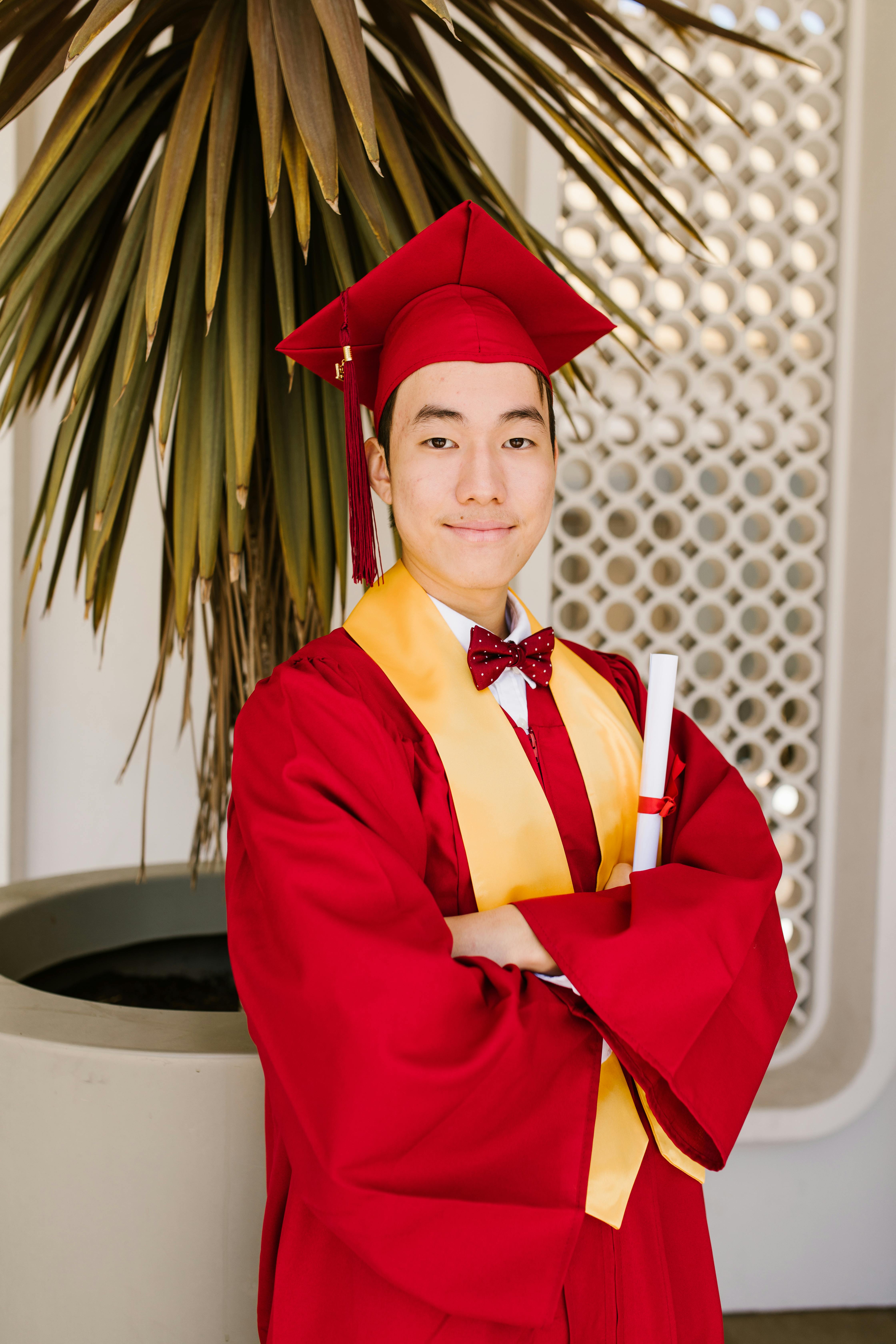 Confident young graduate smiling in red cap and gown, holding diploma.