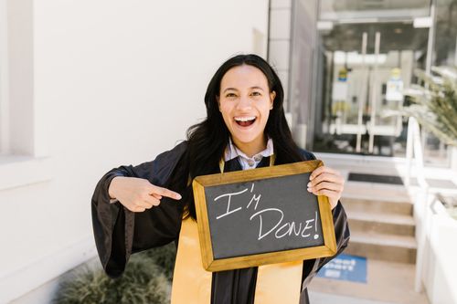 Free Happy woman in graduation gown holding 'I'm done!' sign, celebrating success. Stock Photo