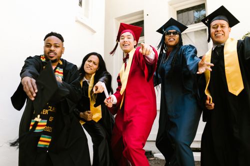 Free Cheerful graduates celebrating their success in colorful gowns outdoors. Stock Photo