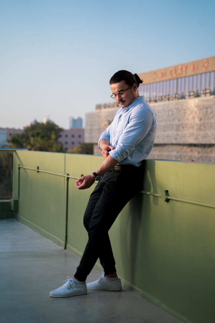 Man Leaning On Concrete Railing While Rolling His Sleeve