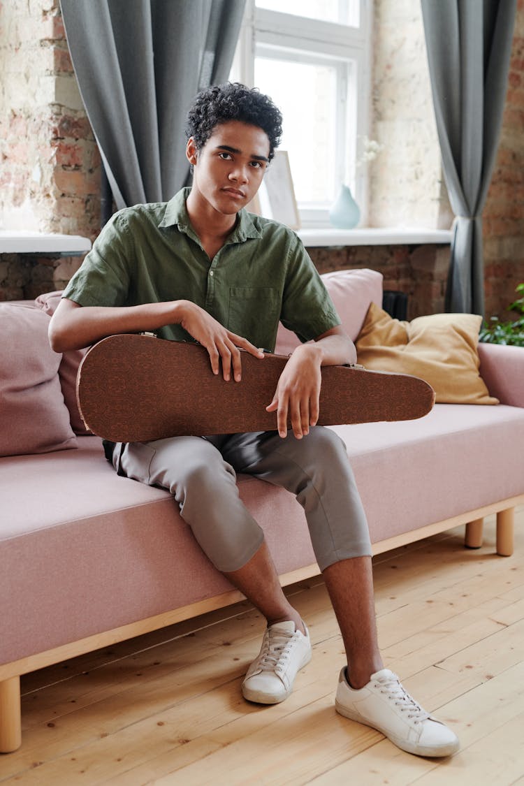 A Man Sitting On Sofa Holding A Violin Case