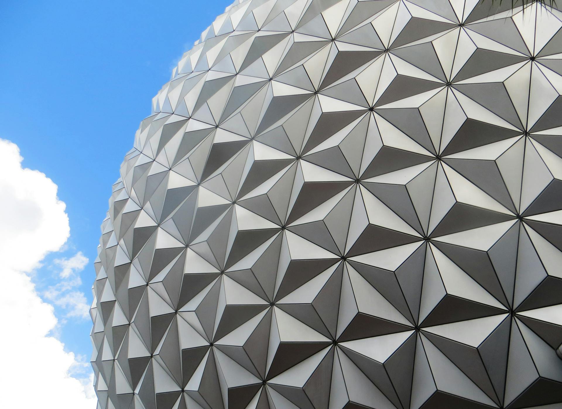 Close-up of a futuristic geometric pattern on a dome against a vibrant blue sky with clouds.