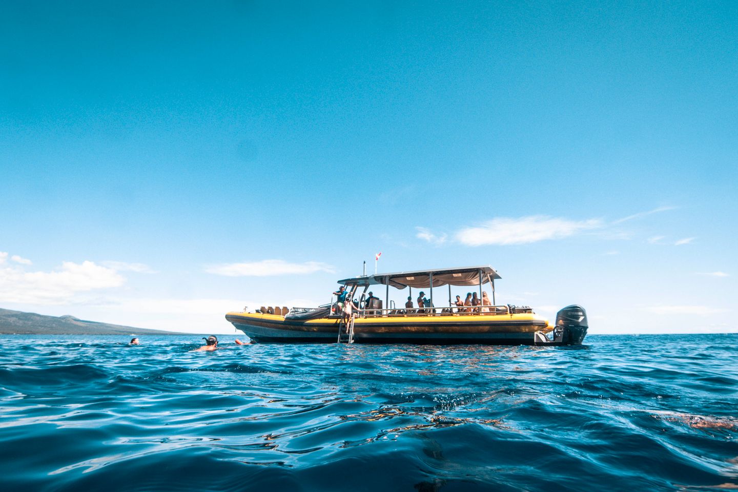 A snorkel boat anchored in open blue water off Maui with swimmers alongside