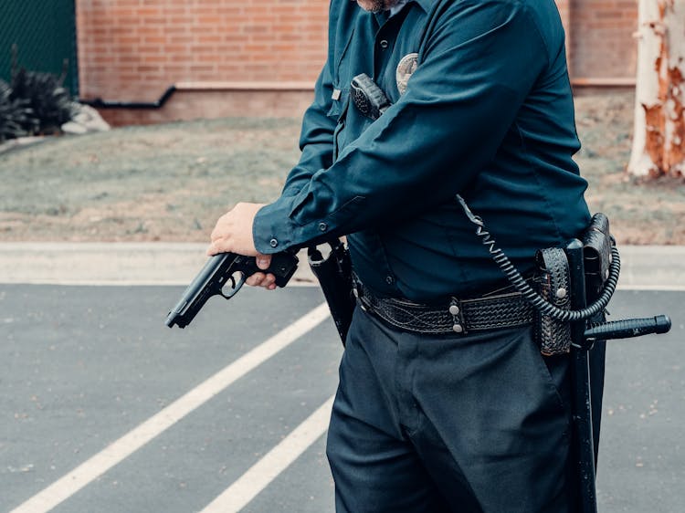 A Person In Police Uniform Holding Black Gun