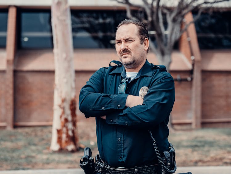 Man In Black Long Sleeve Police Uniform Standing Near Brown Tree